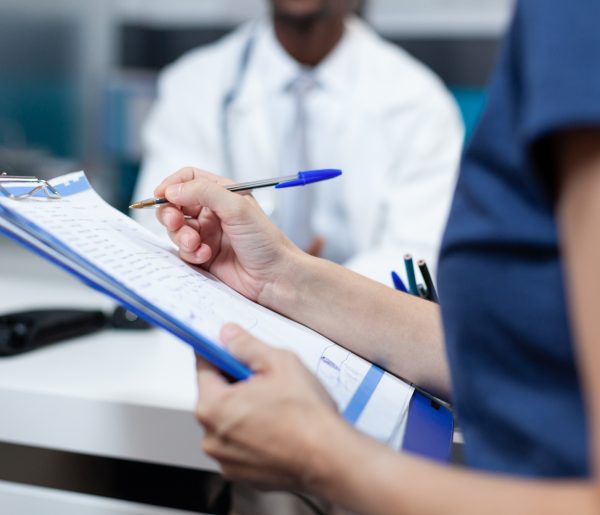 Closeup of patient mother writing medical information on document discussing sickness symptoms with african american doctor during clinical appointment in hospital office. Health care service